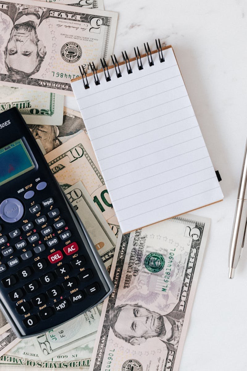 Flat lay of US dollar bills with calculator and notebook for budgeting.