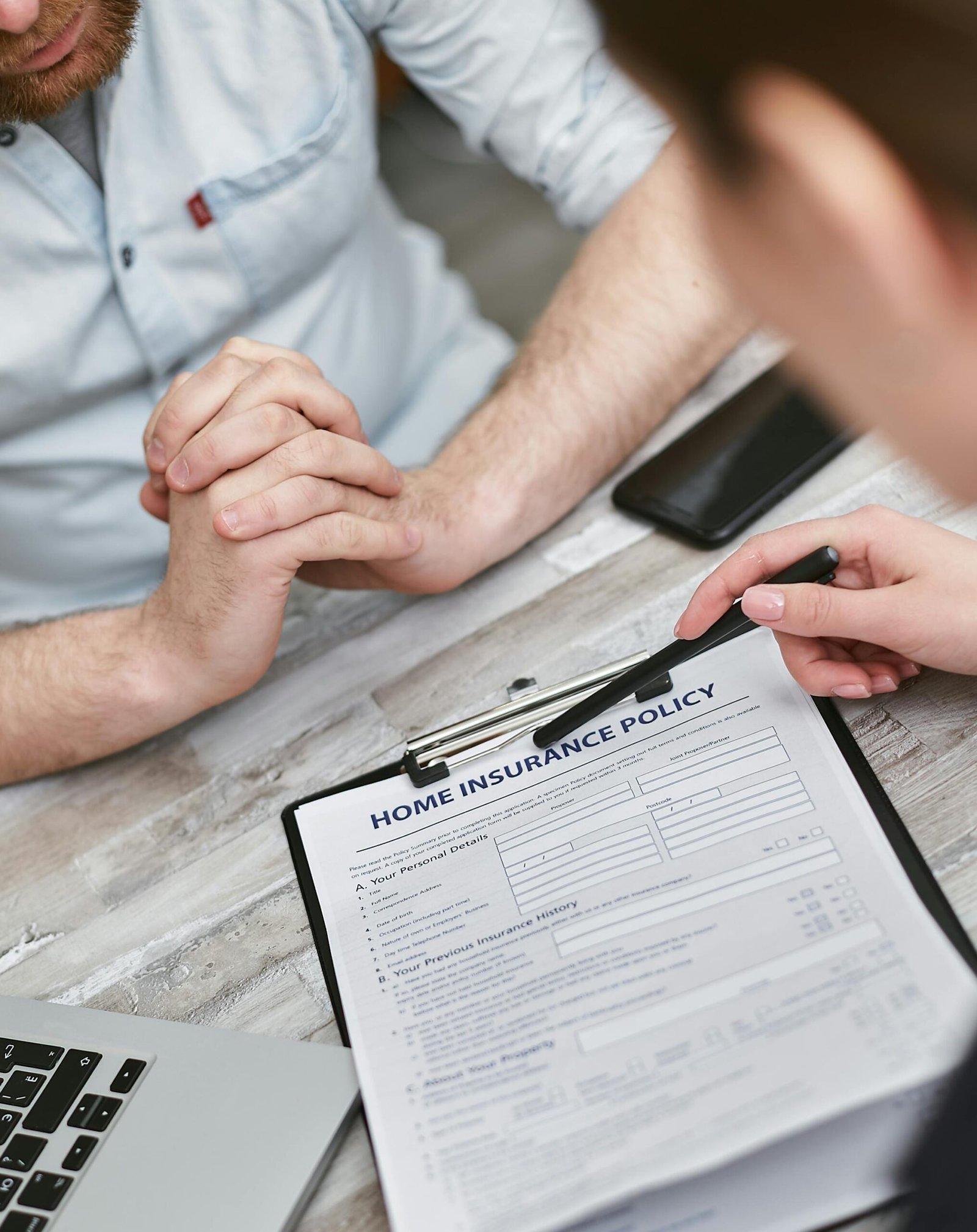 Two adults reviewing a home insurance policy document on a table with electronic devices.